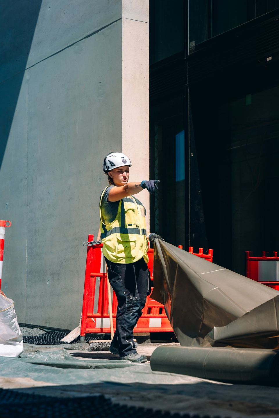 Bauarbeiter mit Helm und Warnweste zieht eine Plane auf der Baustelle der Uniq Towers
