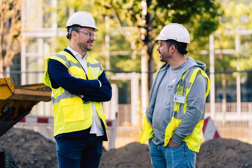 Zwei Mitarbeiter in Warnwesten im Gespräch auf der Baustelle
