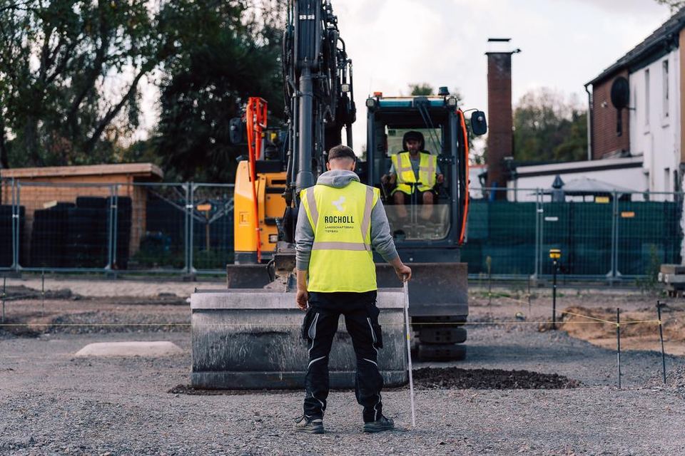 Mitarbeiter in Warnweste vor einem Bagger auf der Baustelle